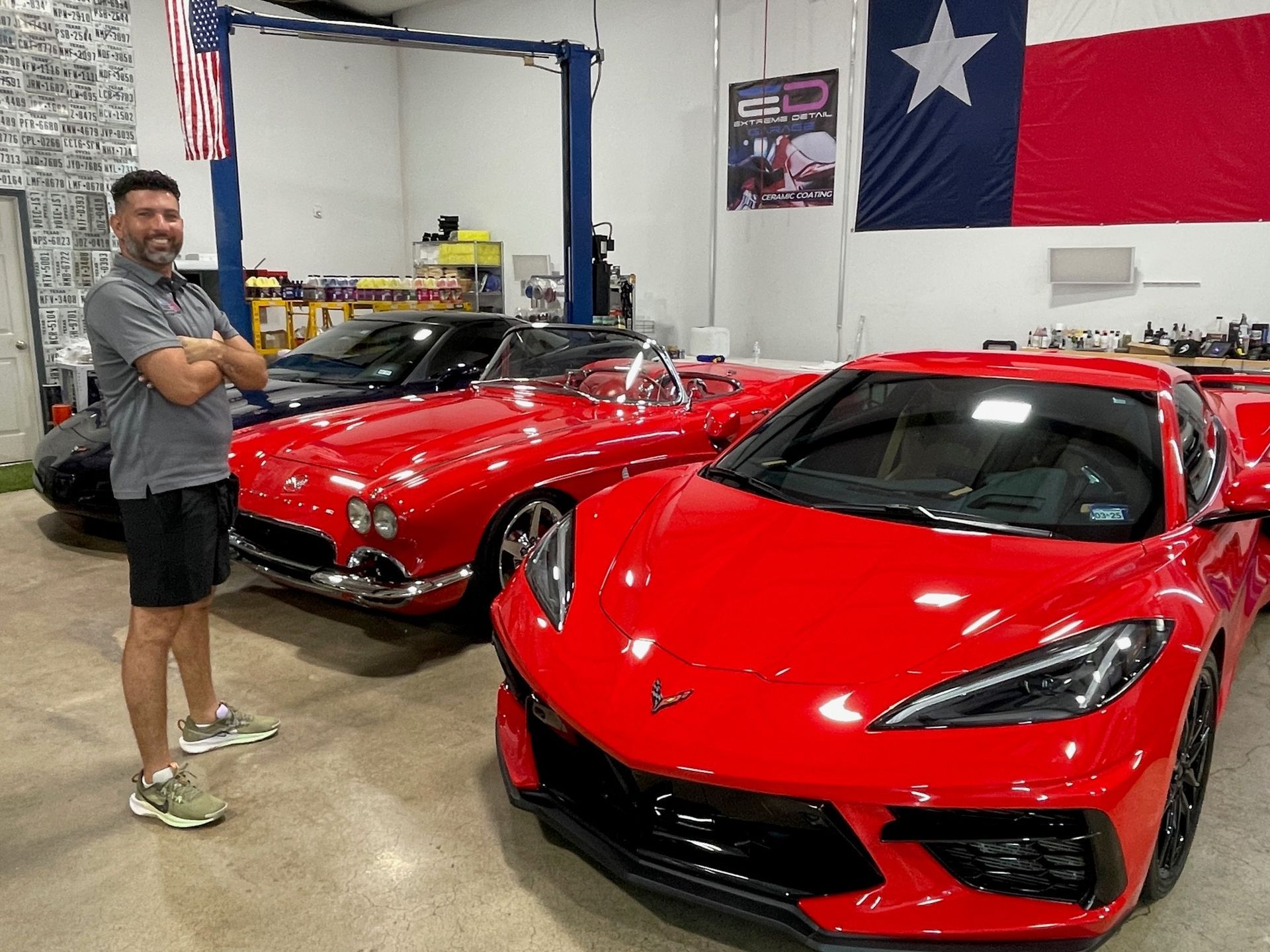A man is standing next to two red sports cars in a garage.