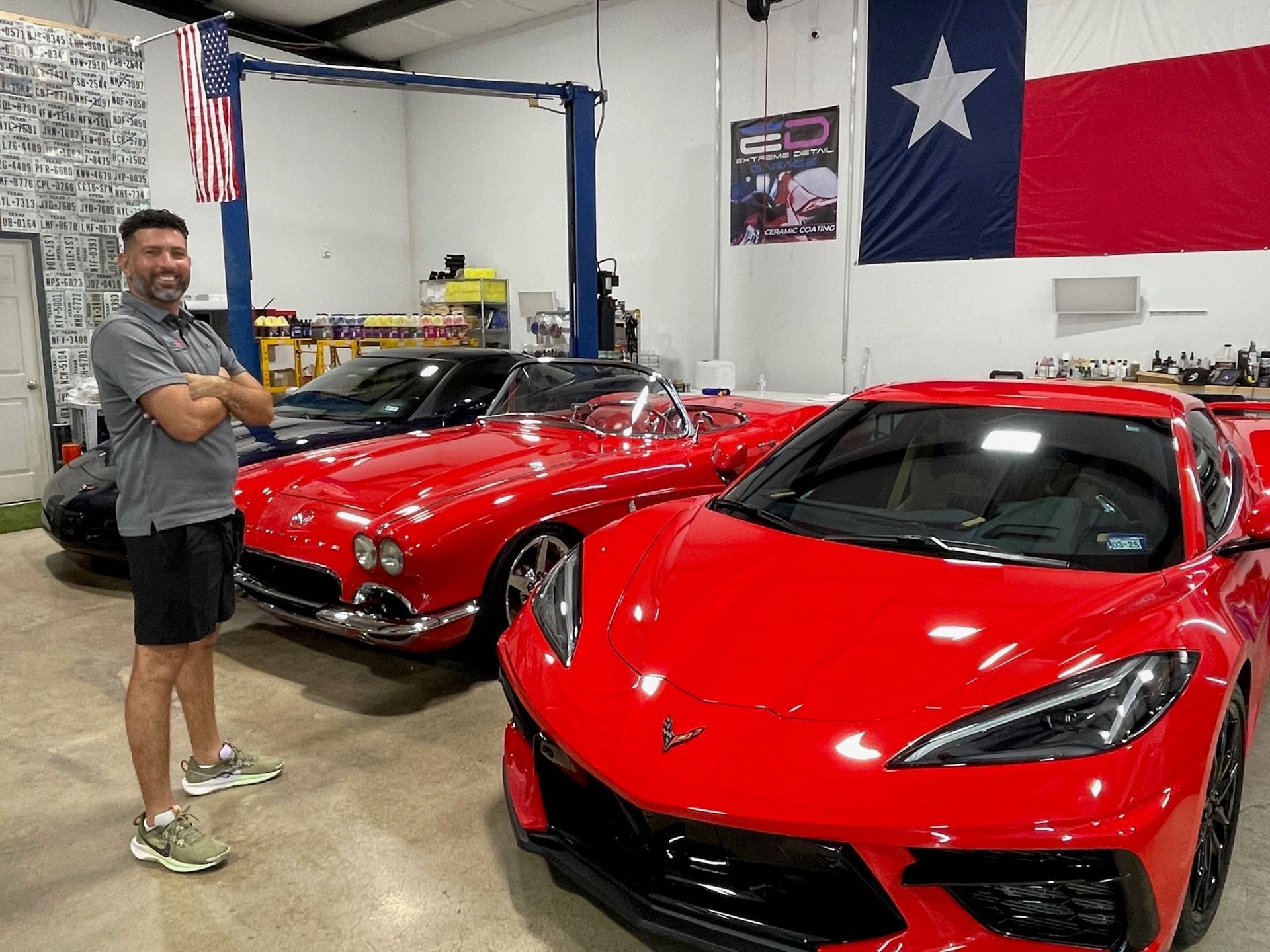 A man is standing in front of two red sports cars in a garage.
