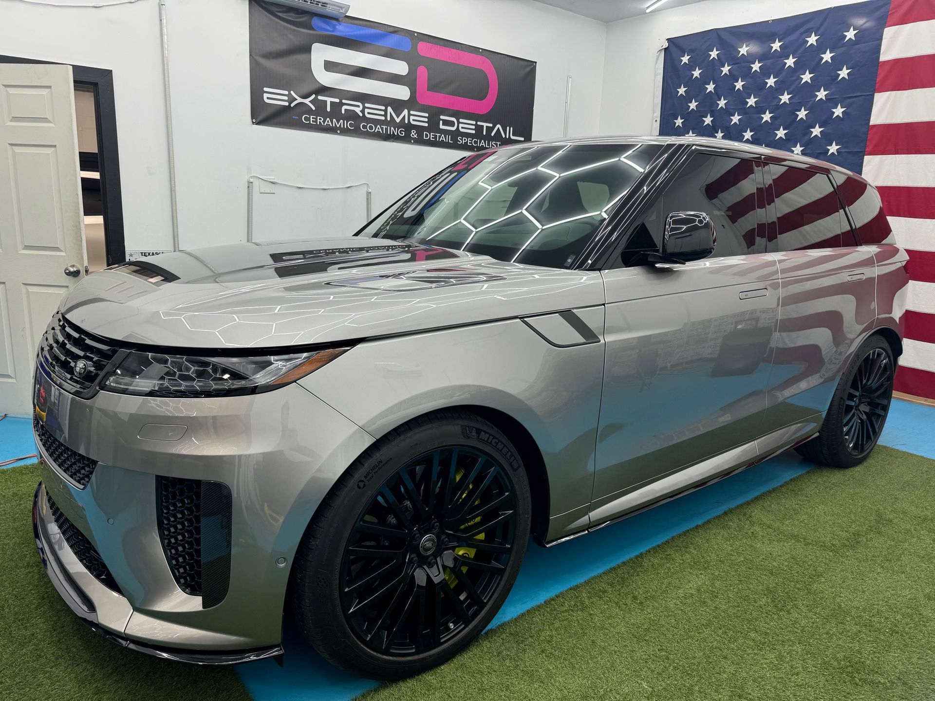 A silver range rover is parked in front of an american flag.