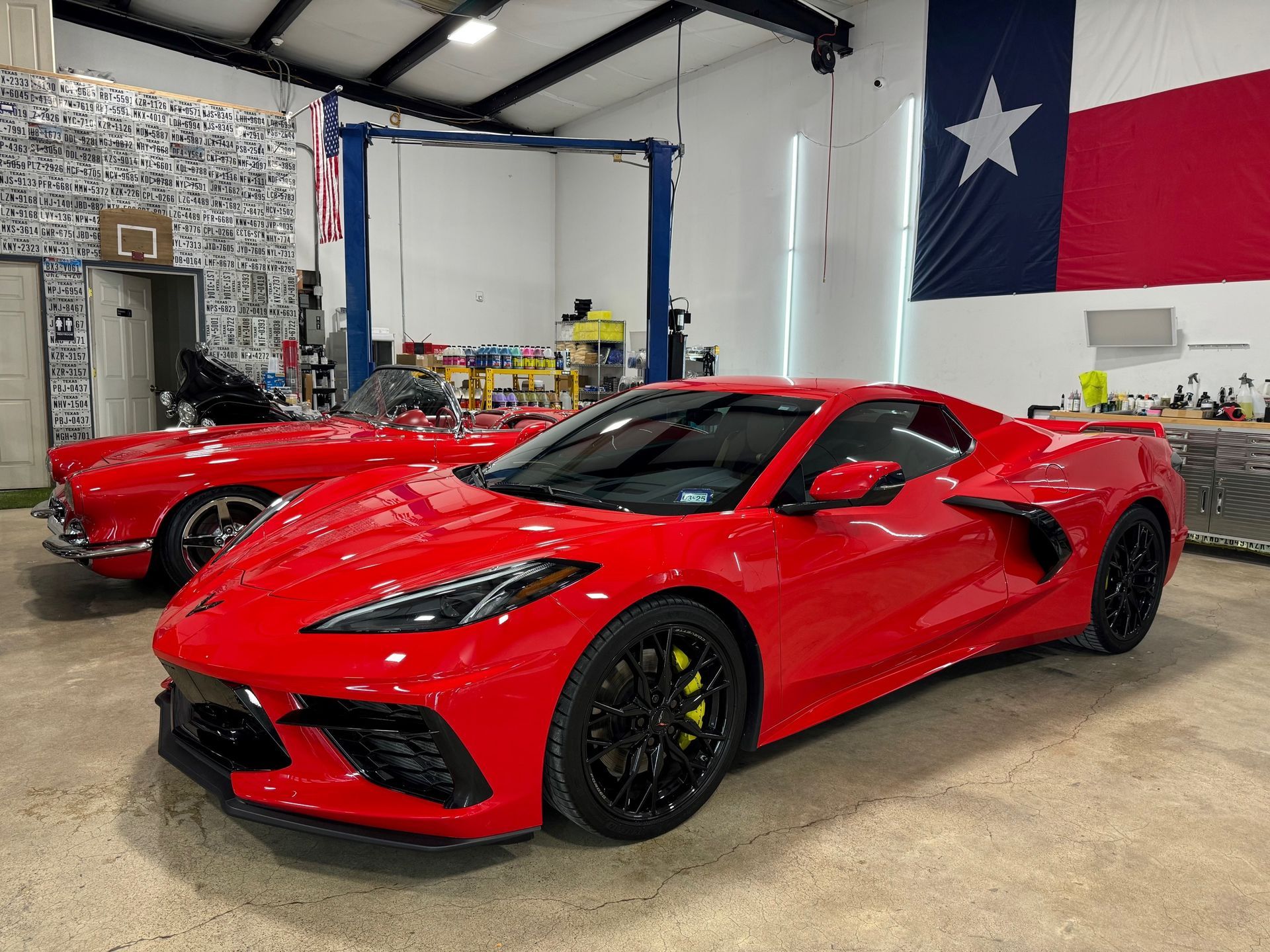 Two red sports cars are parked in a garage next to a texas flag.