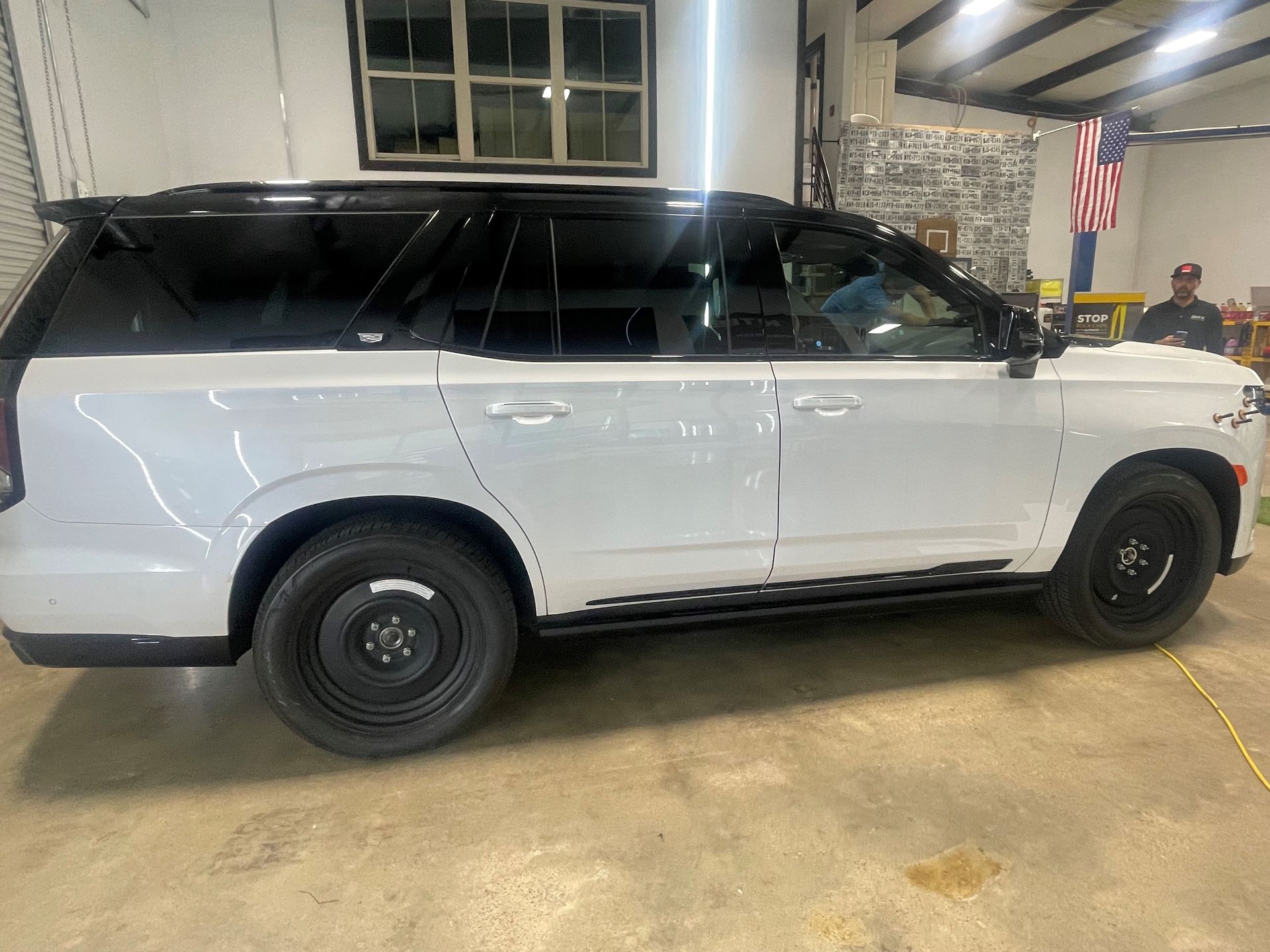 A white suv is parked in a garage next to an american flag.