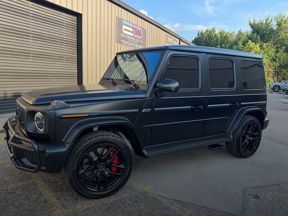 Black Mercedes-Benz G-Class SUV with tinted windows and black rims parked outside a building.