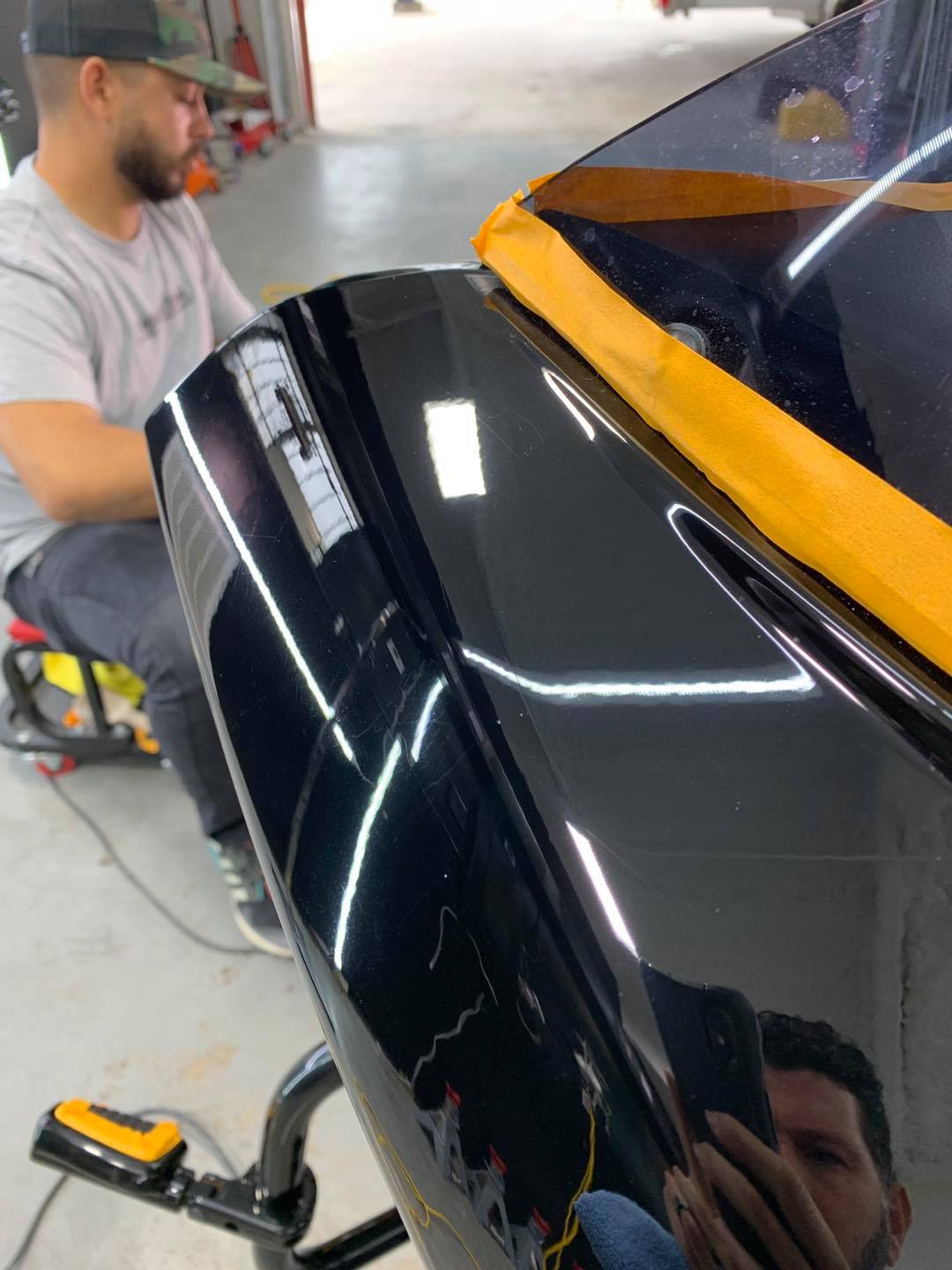 A man is sitting on a stool working on a black car.