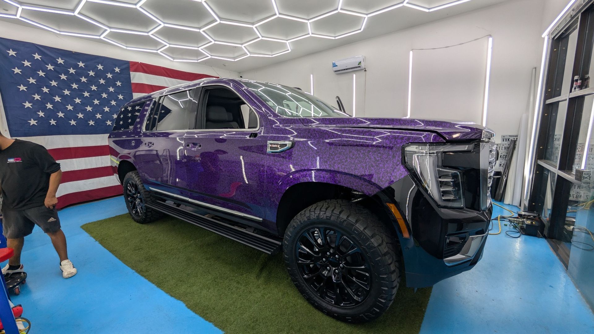 A purple truck is parked in a garage next to an american flag.
