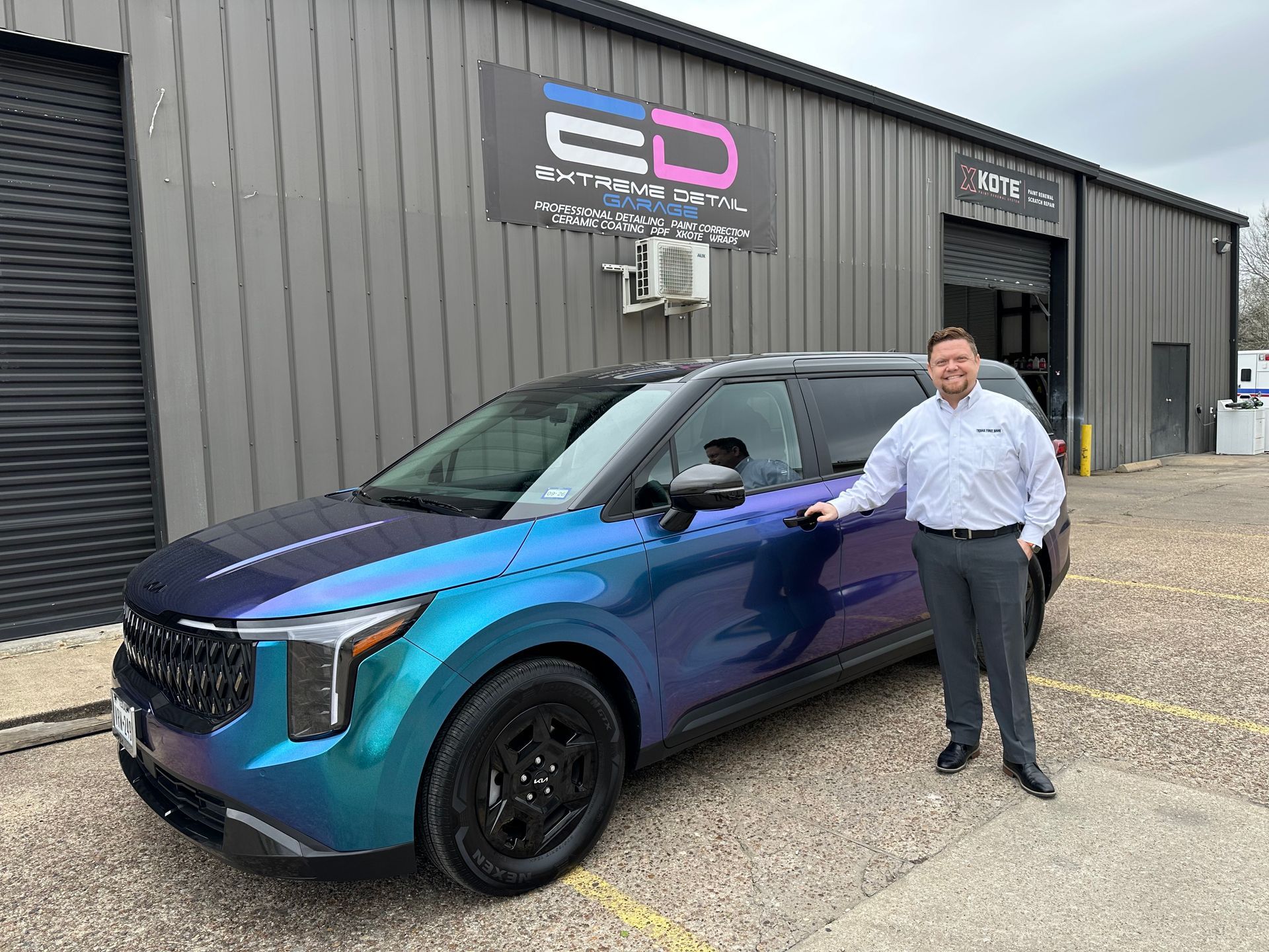 A man is standing in front of a purple and blue car.