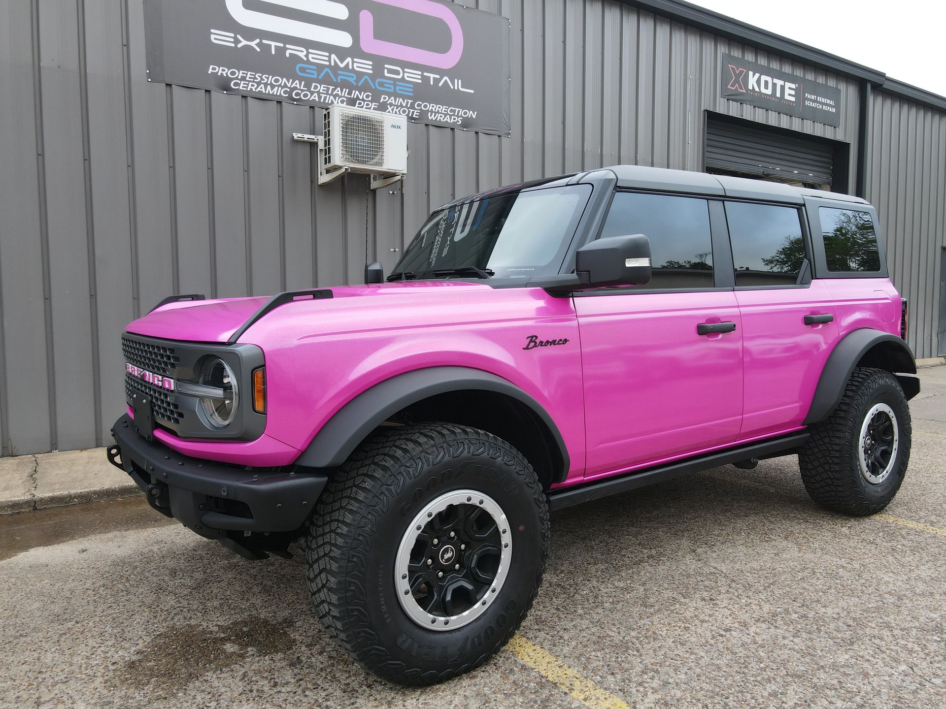 A pink ford bronco is parked in front of a building.