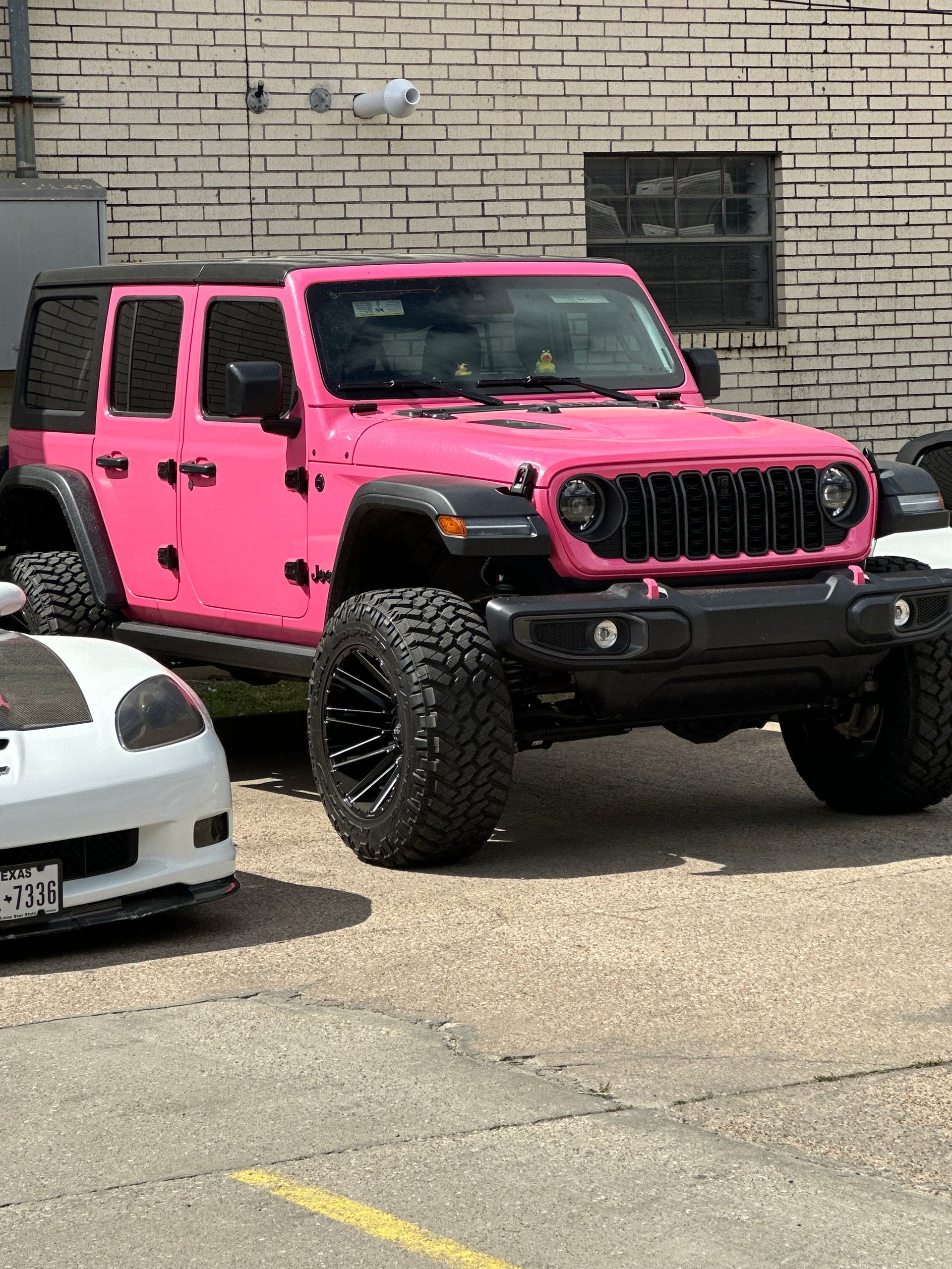 A pink jeep is parked next to a white car in a parking lot.