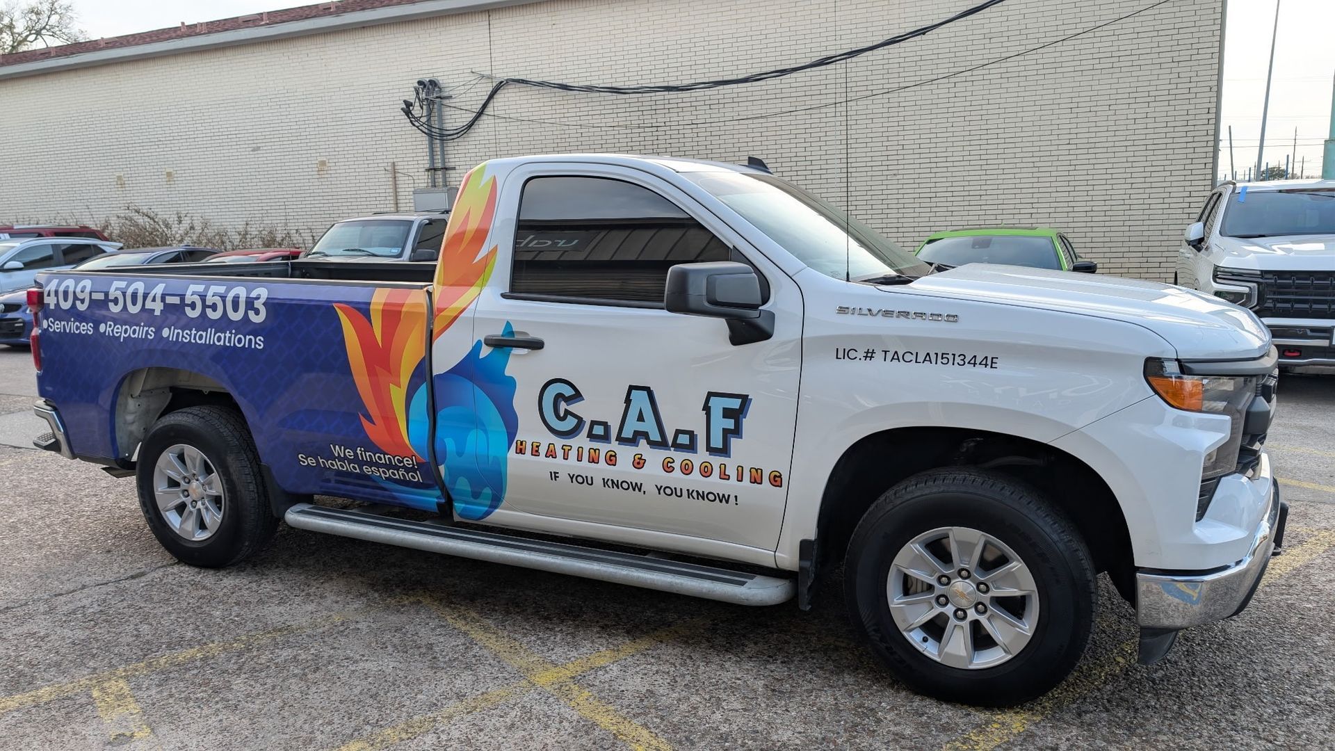 White and blue Chevrolet pickup truck with business graphics, parked outdoors.