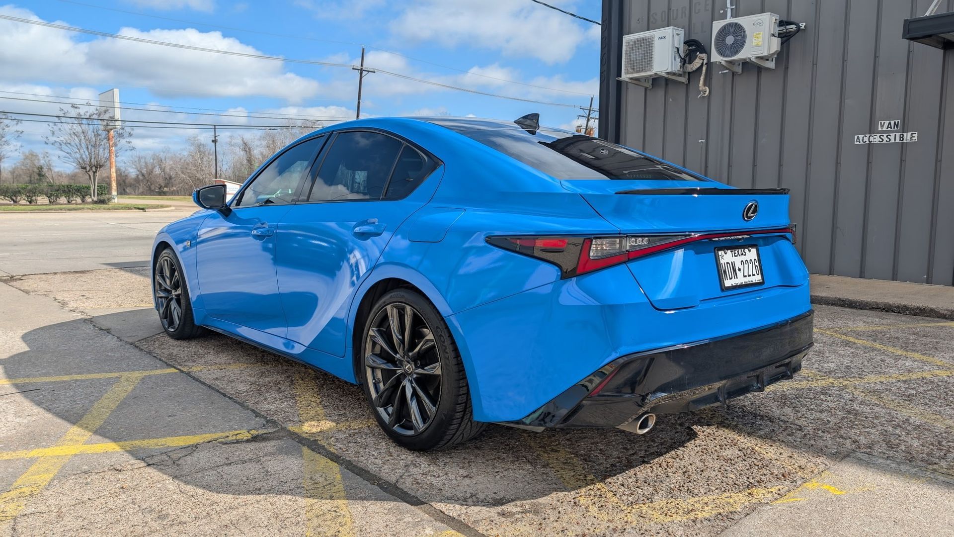 Blue Lexus sedan parked on asphalt in front of a building on a sunny day.