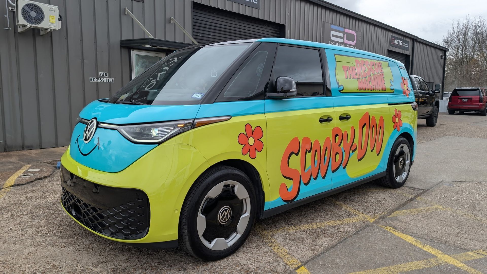 Scooby Doo-themed Volkswagen ID. Buzz van in teal and yellow parked in front of a building.