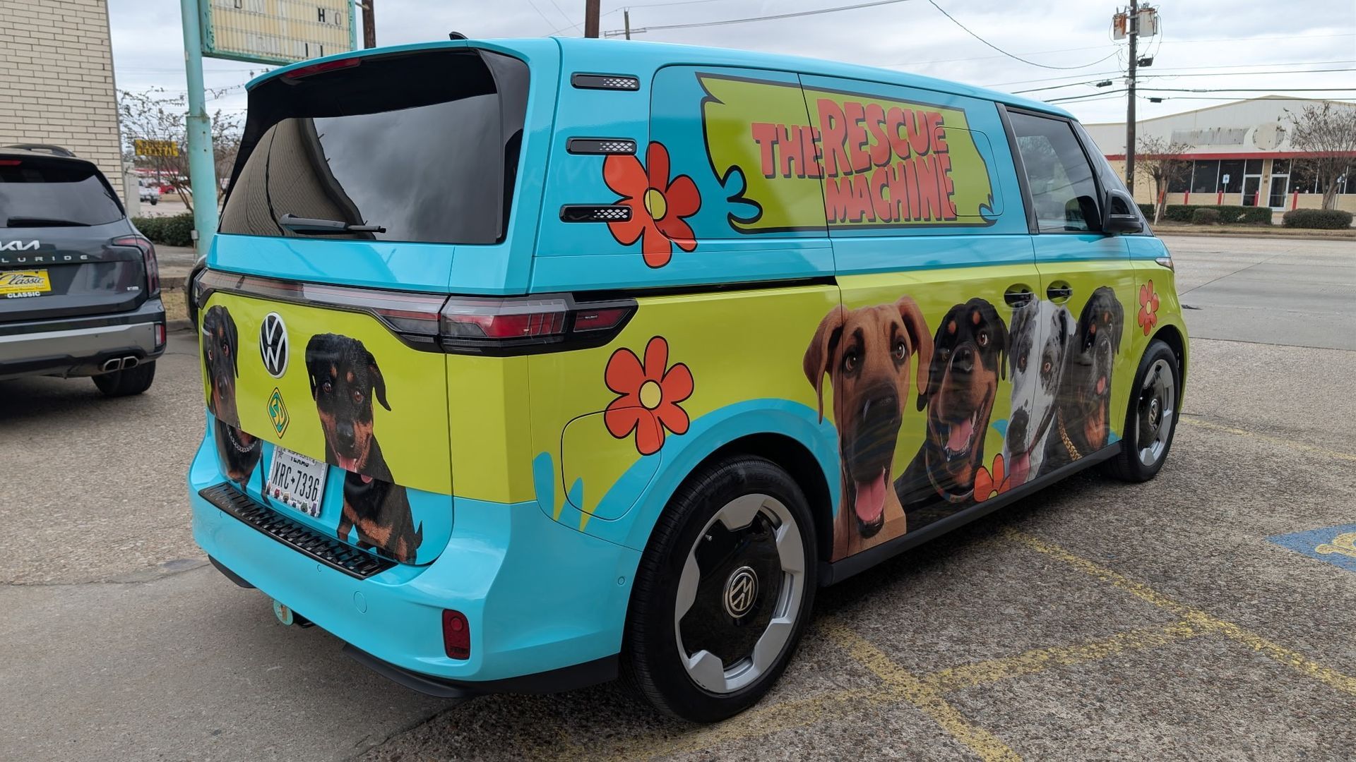 Turquoise Mystery Machine van with dog portraits; parked on street.