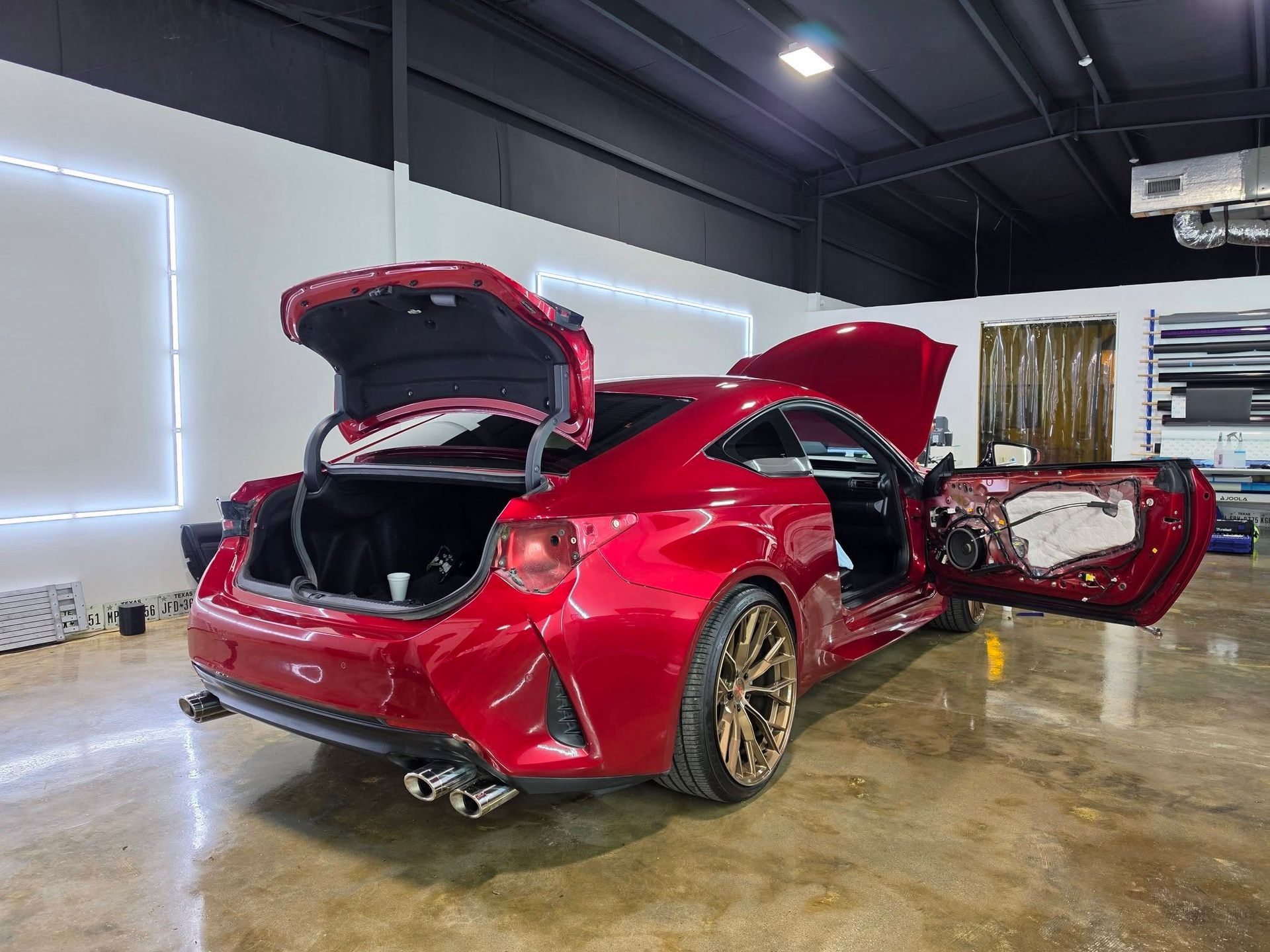 Red sports car with trunk and passenger door open in a garage showroom