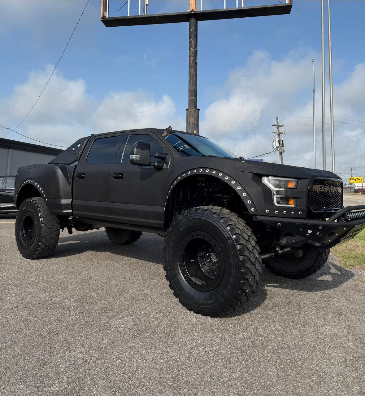 Black lifted pickup truck parked on gravel under a roadside sign against a blue sky.