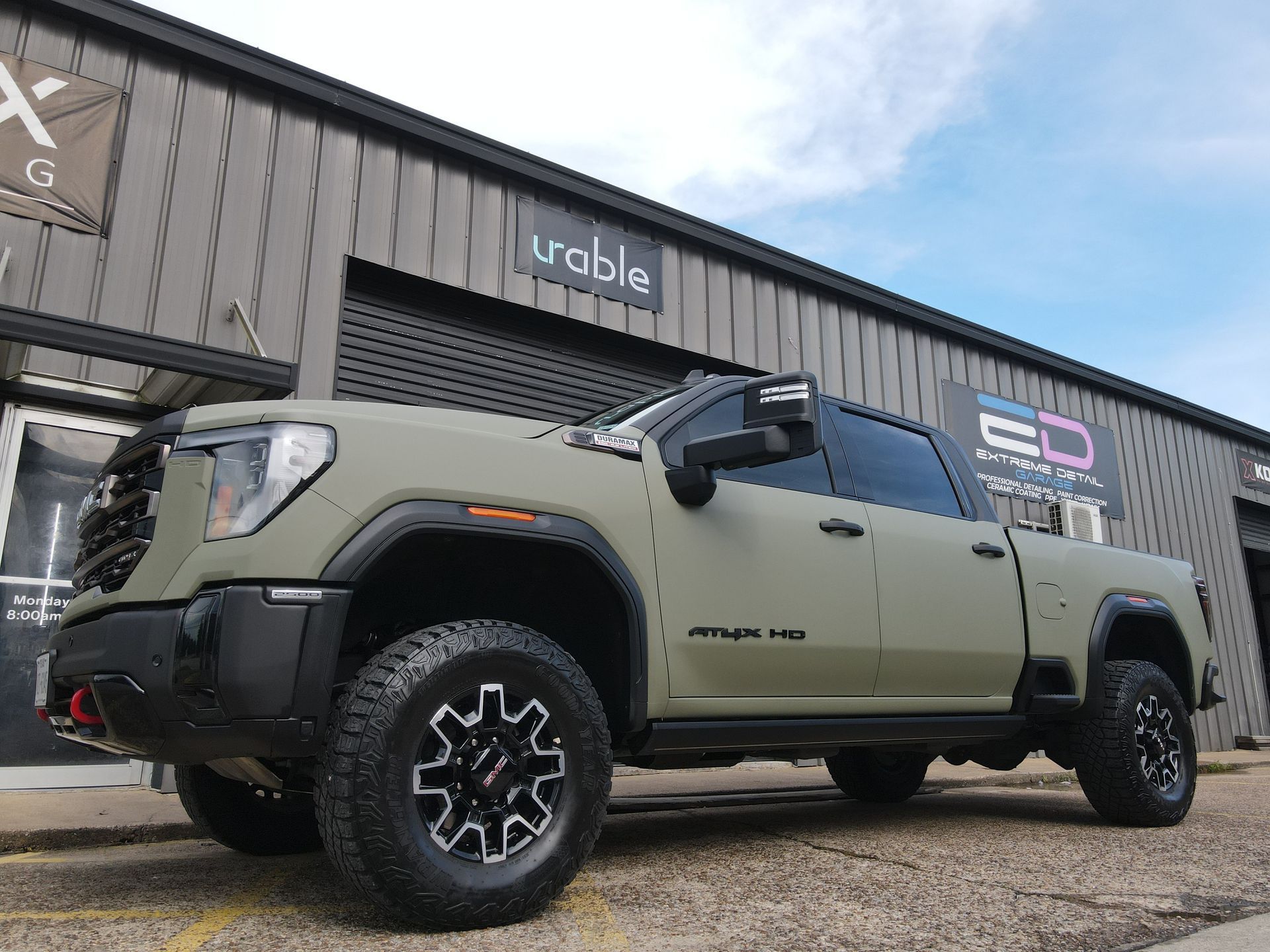 A green truck is parked in front of a building.