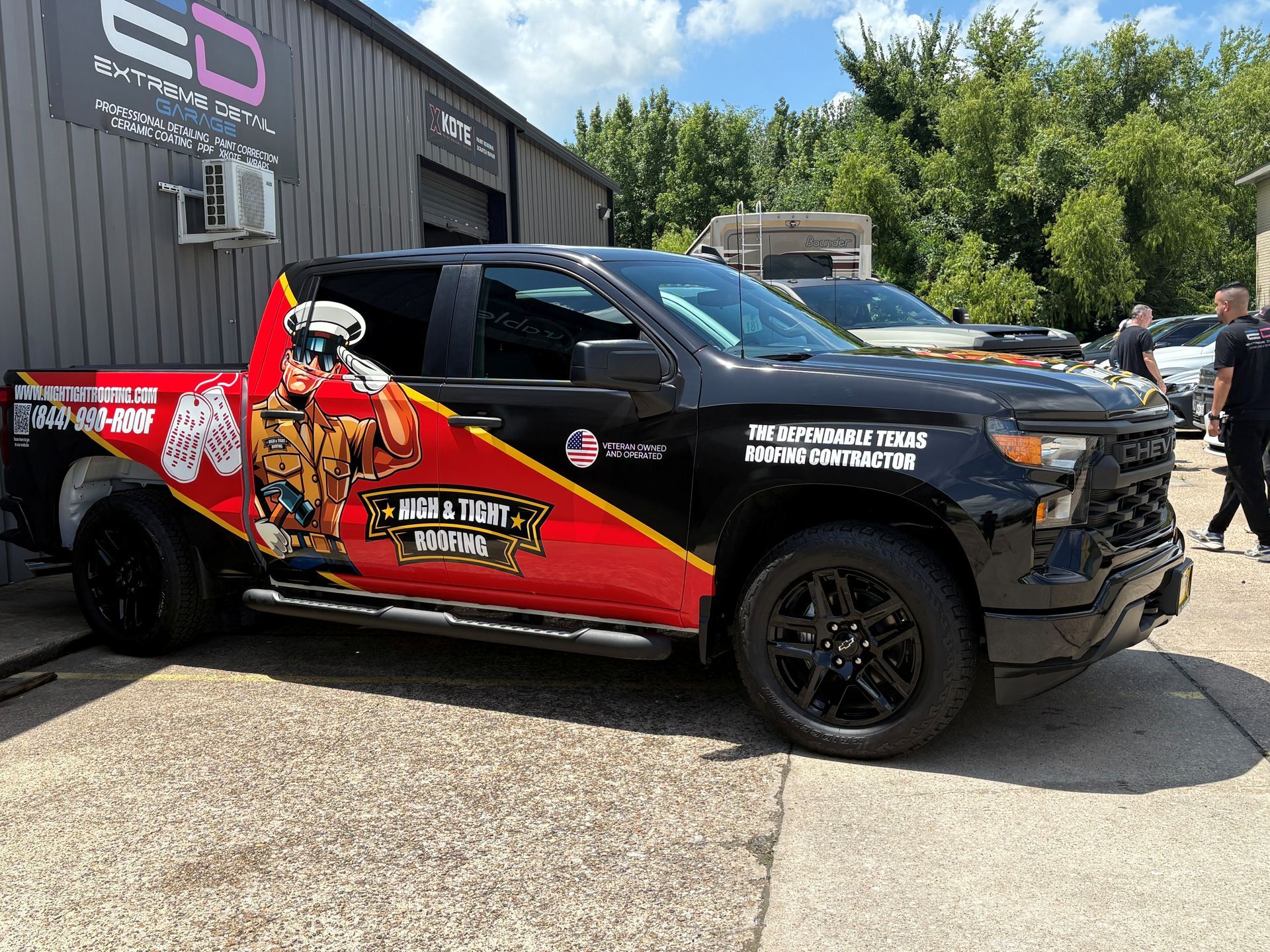 A black truck with a red and yellow wrap is parked in front of a building.