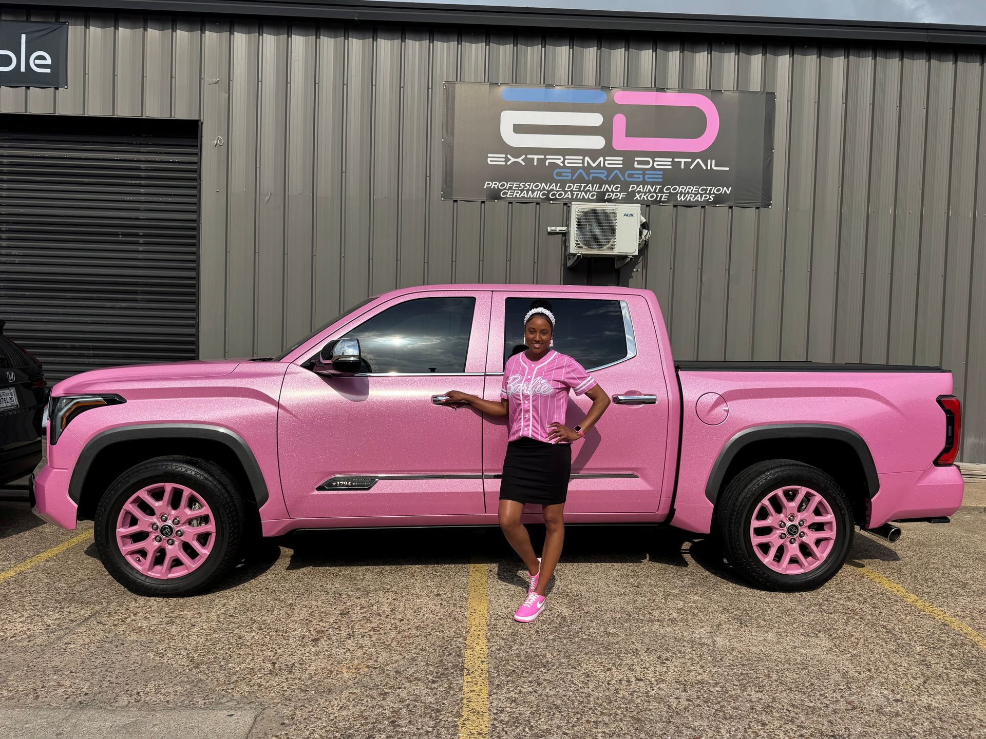 A woman is standing in front of a pink truck.