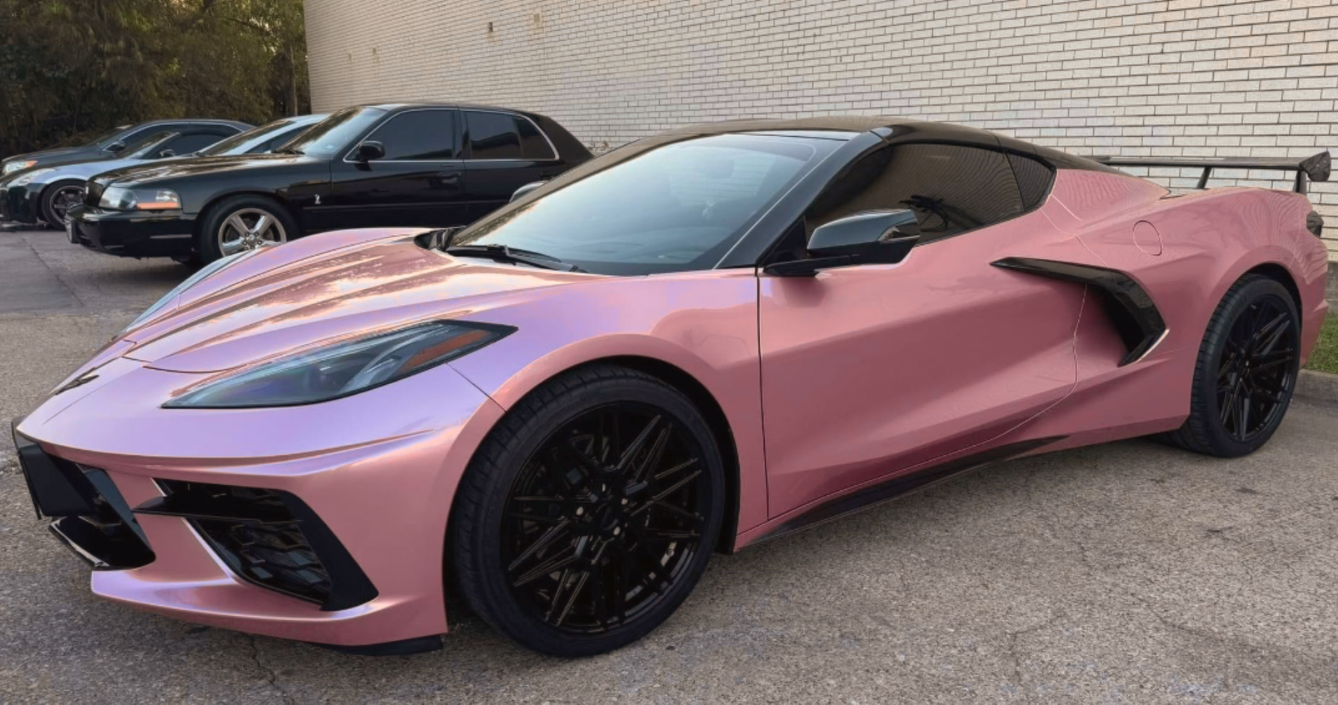 A pink corvette is parked in a parking lot next to other cars.