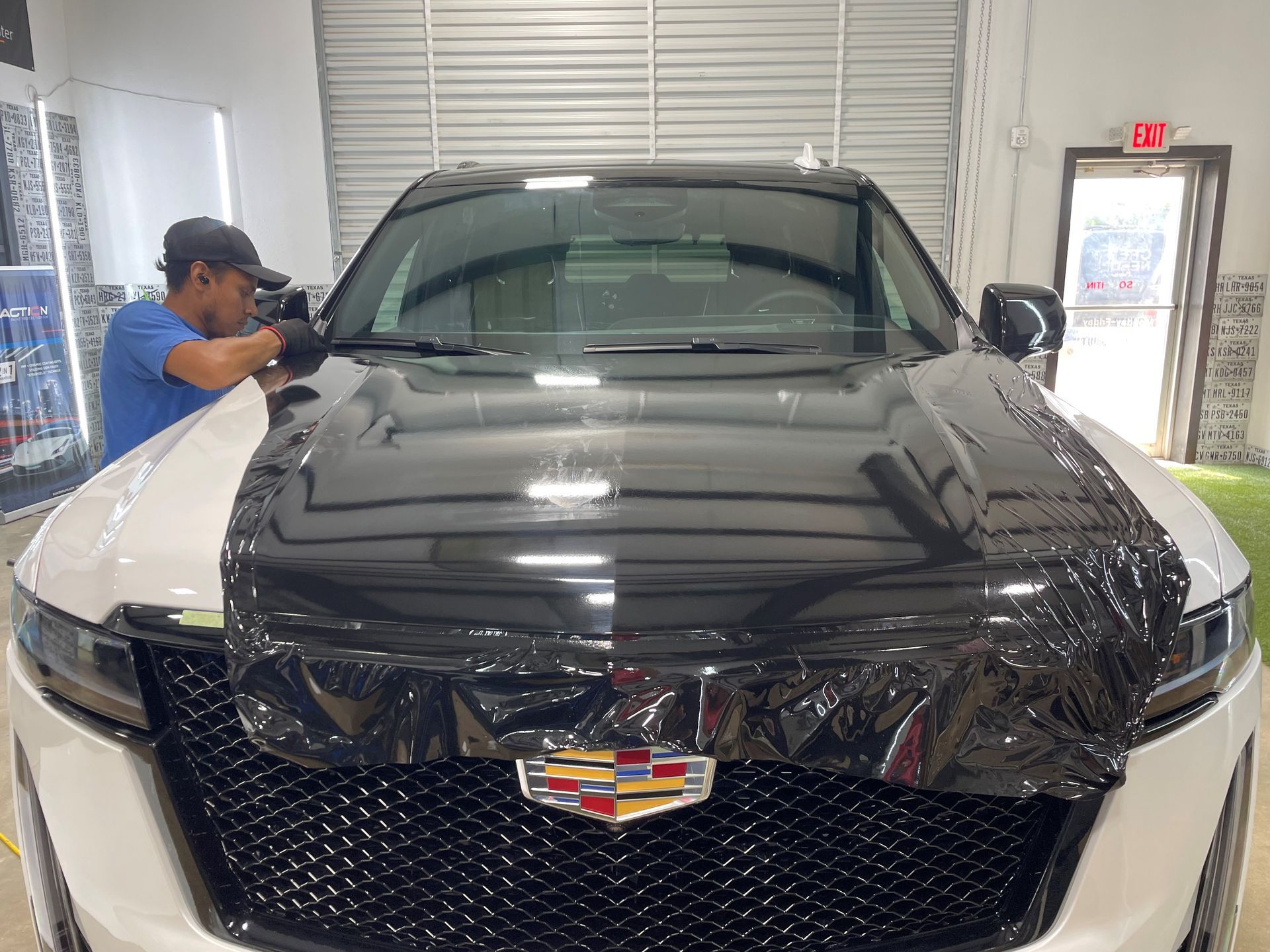 A man is wrapping the hood of a black cadillac escalade.