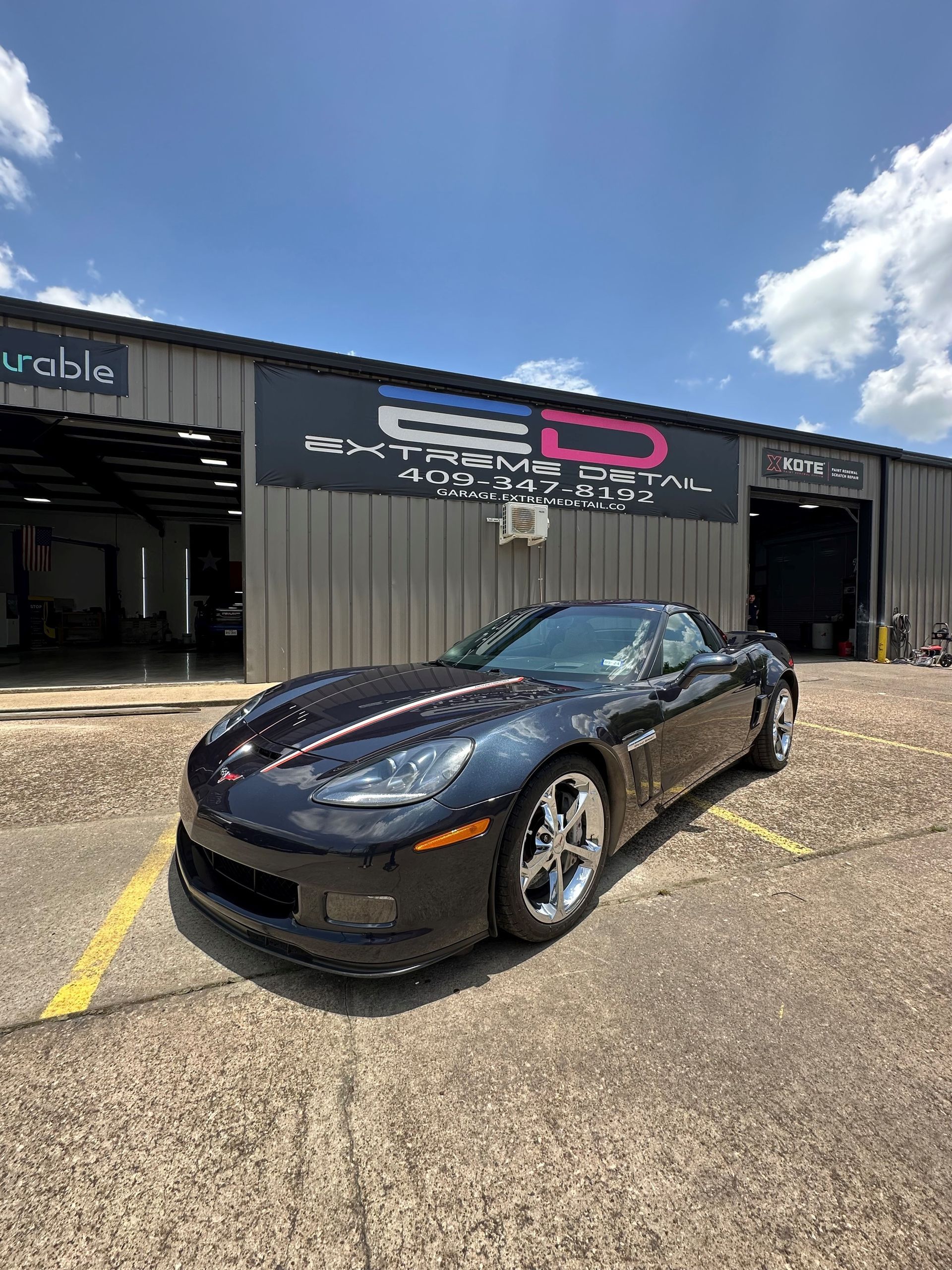 A black corvette is parked in a parking lot in front of a building.