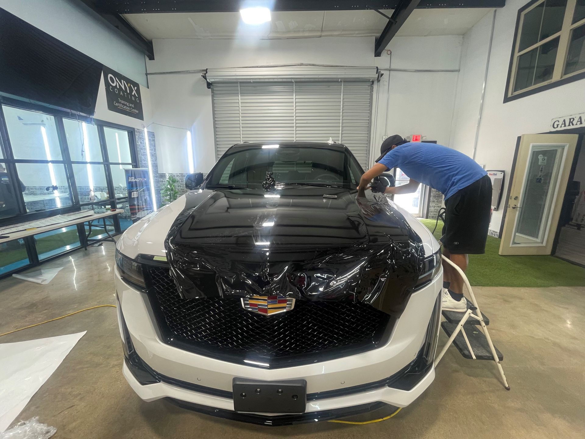 A man is cleaning the hood of a black and white car in a garage.
