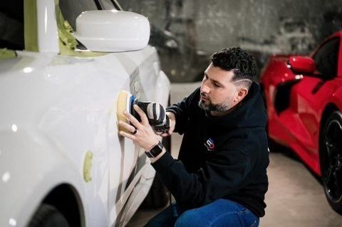 A man is polishing a white car in a garage.