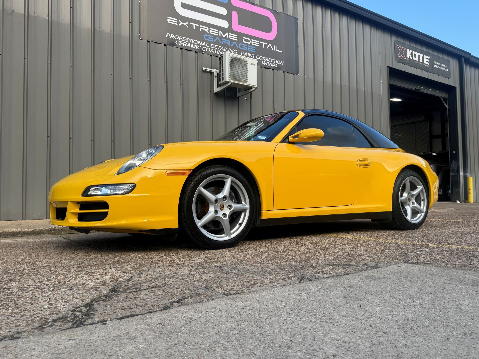 A yellow porsche 911 is parked in front of a building.