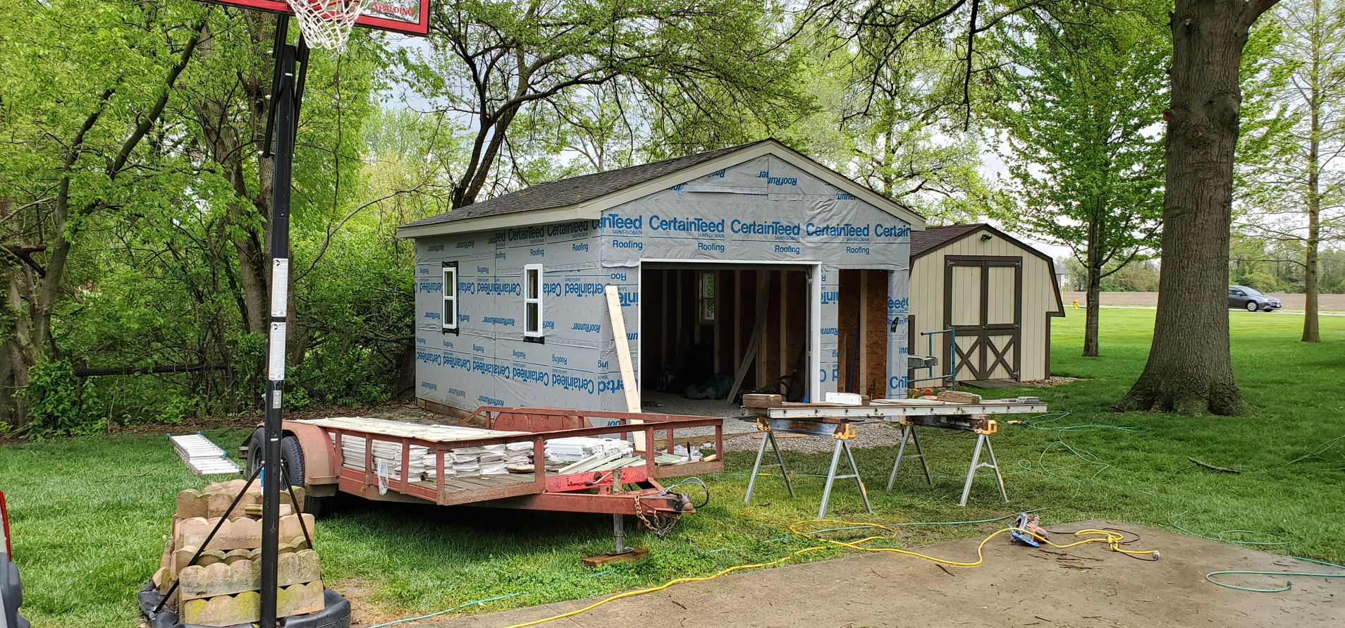 A small house is being built in a yard next to a basketball hoop.