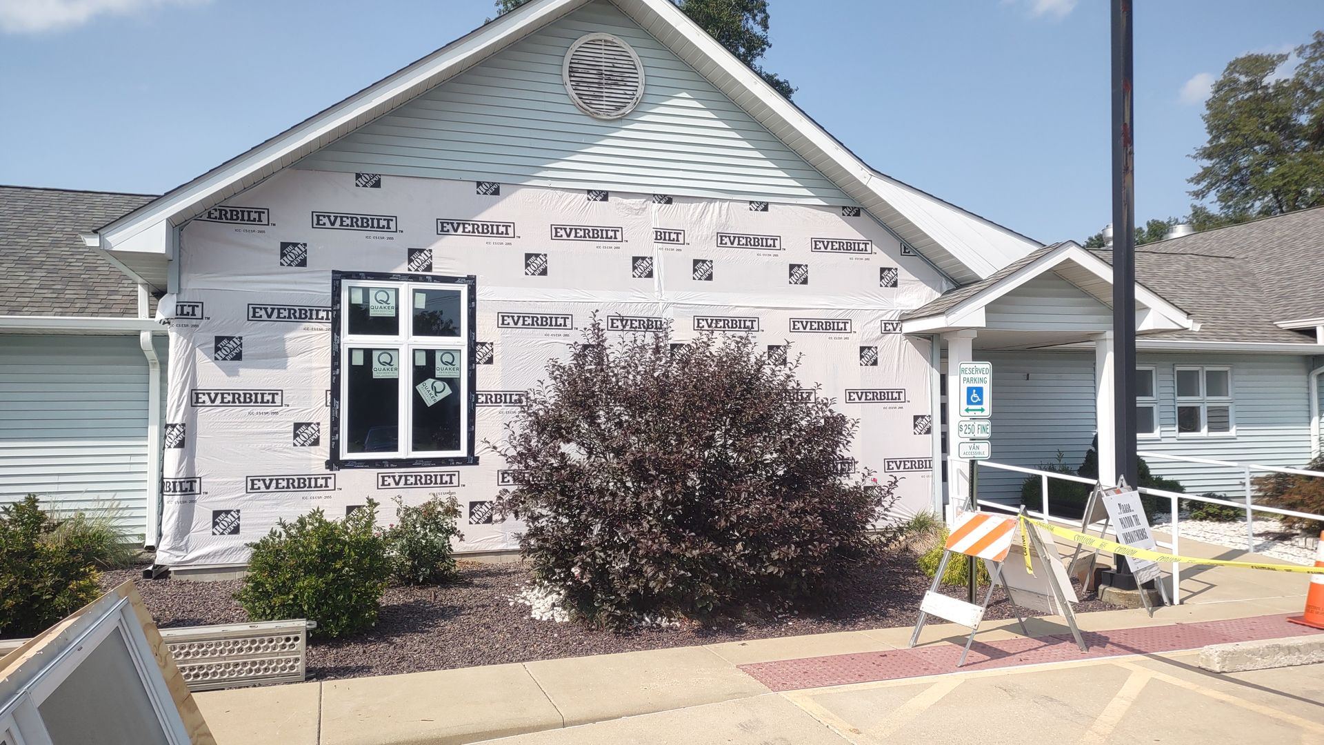 Building exterior under renovation. White sheathing exposed; blue, white, and gray siding. Construction barriers present.
