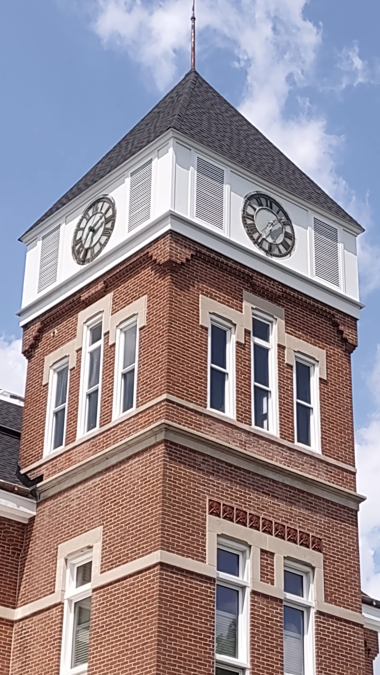 Brick clock tower with two clocks, white accents, and a black roof.