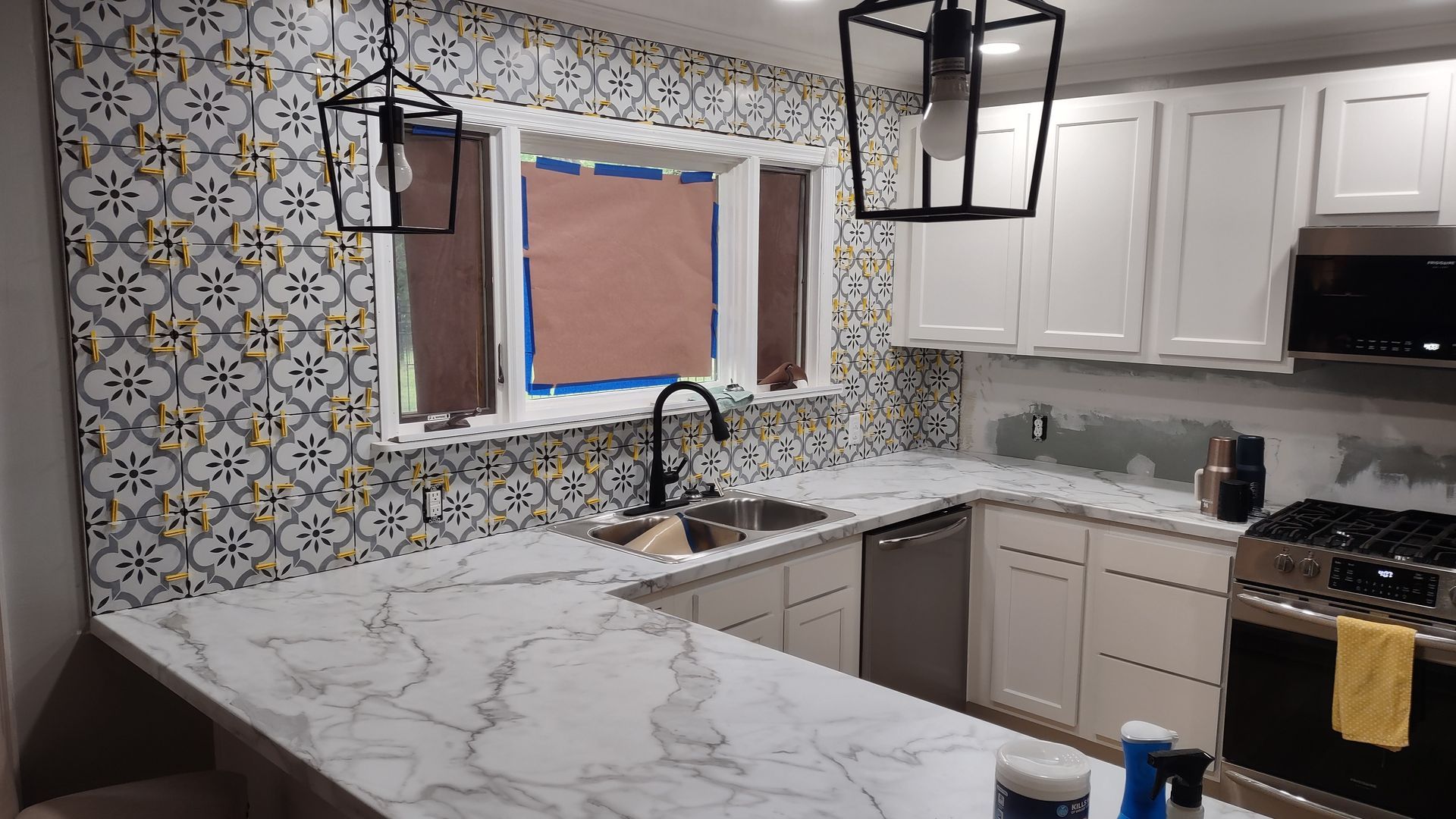 Kitchen with patterned backsplash, marble countertops, white cabinets, and black accents.