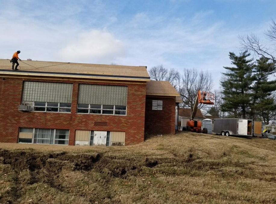 A brick building with a worker on the roof and machinery nearby, likely undergoing construction or demolition.