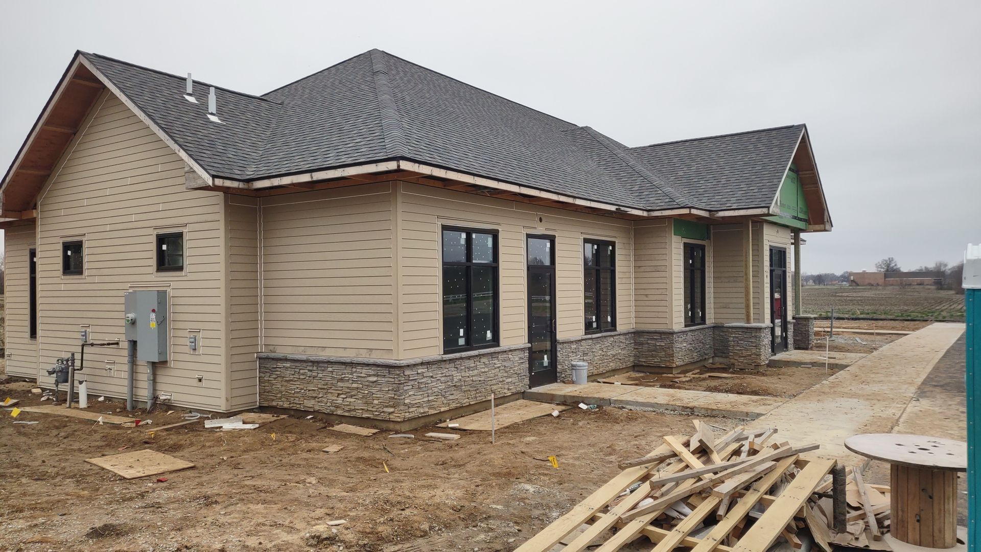 Beige house under construction with black windows, stone accents, and gray roof.