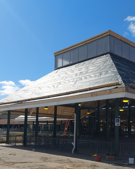 Barn under construction with black tarps on the roof against a blue sky.
