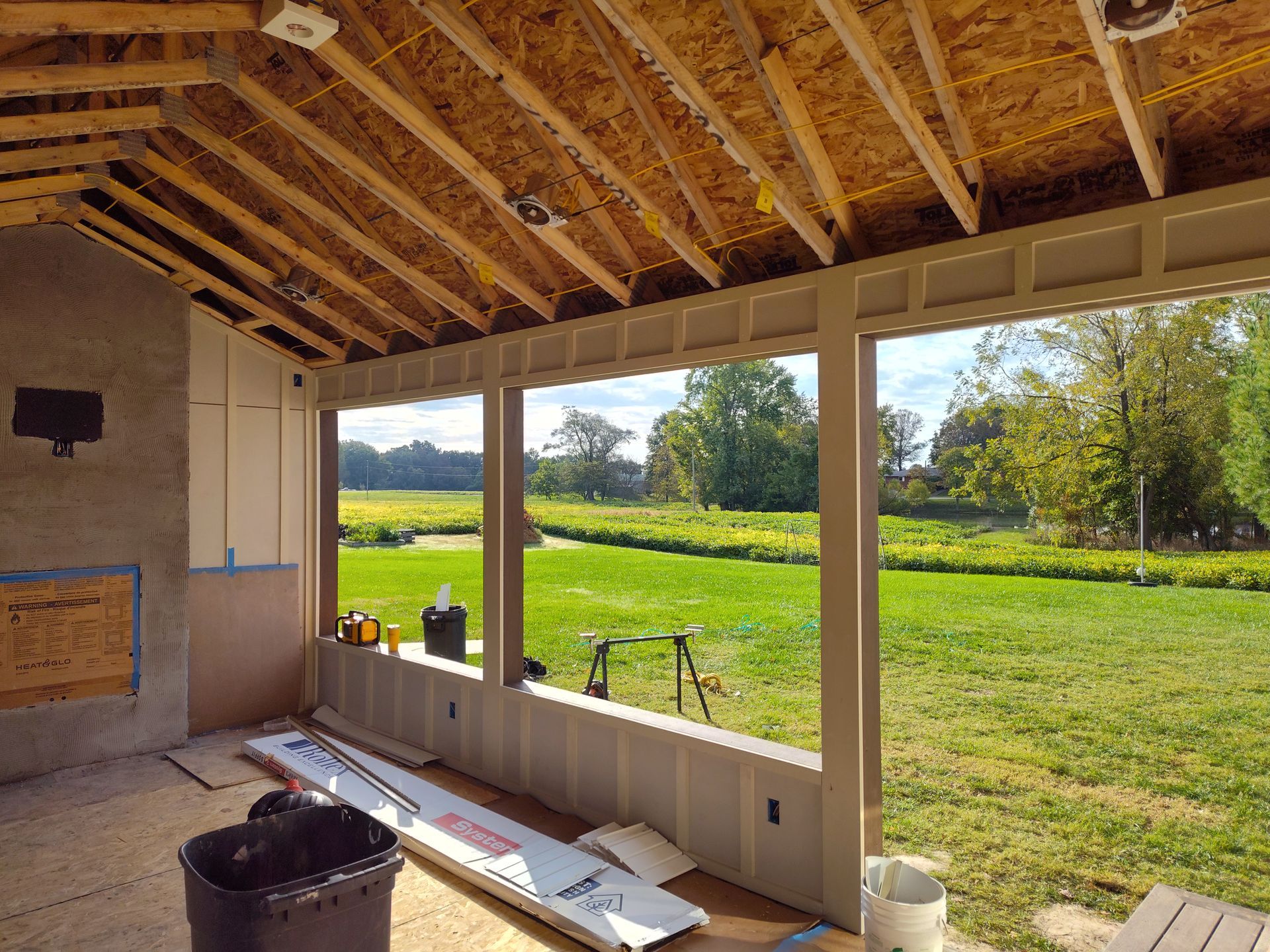 Construction of an outdoor porch with a view of a green field under a blue sky.