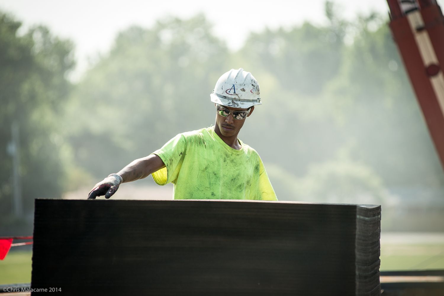 A construction worker wearing a hard hat and safety glasses is holding a large piece of wood.
