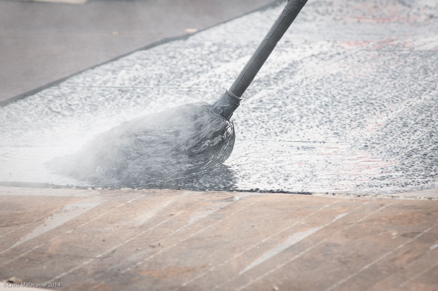 A person is using a high pressure washer to clean a wooden floor.