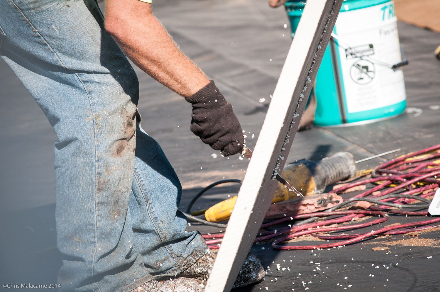 A man is kneeling down and cutting a piece of metal