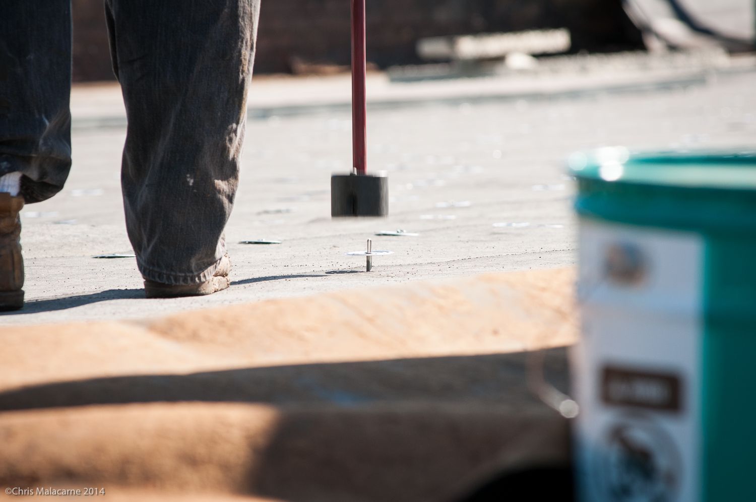 A person is walking on a sidewalk next to a green bucket.