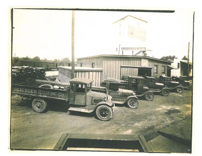 A black and white photo of old trucks parked in front of a building