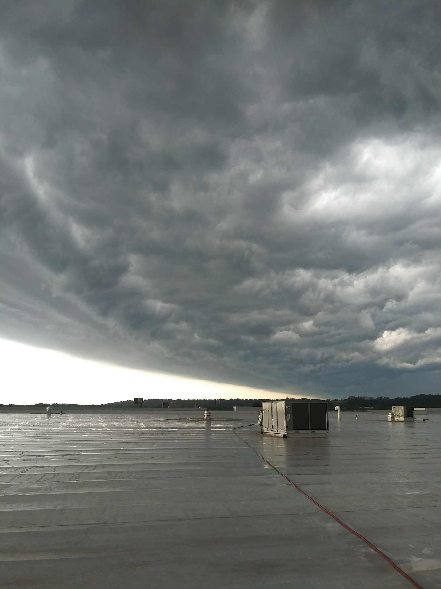 Dark storm clouds rolling over a wet, flat surface, buildings in the distance.