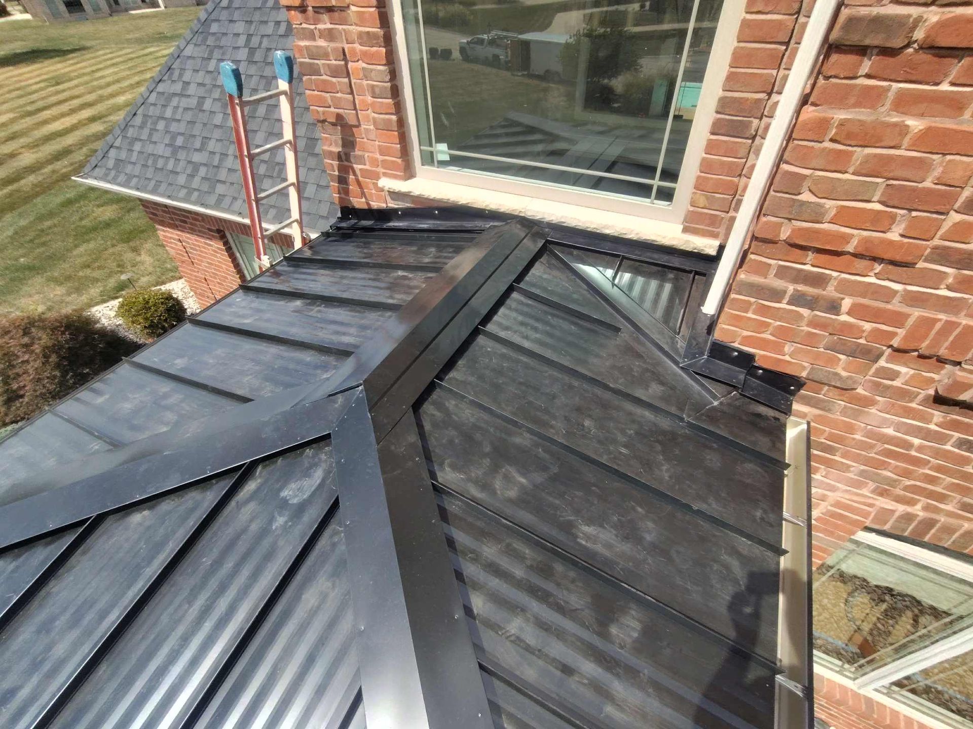 Black metal roof on a brick building with a ladder leaning against the roof.