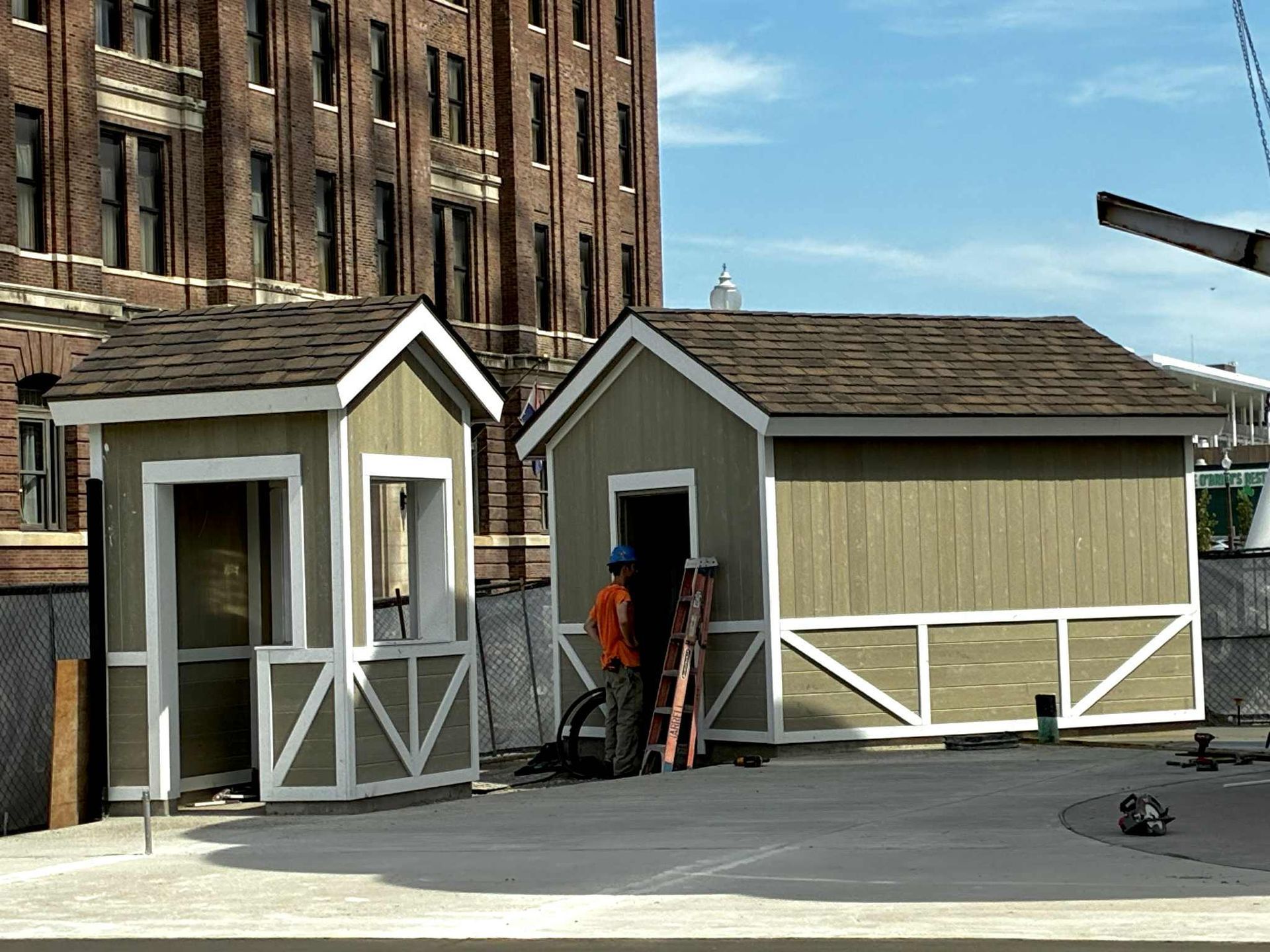 Two small, light green and white sheds, one with person standing, in front of a brick building.
