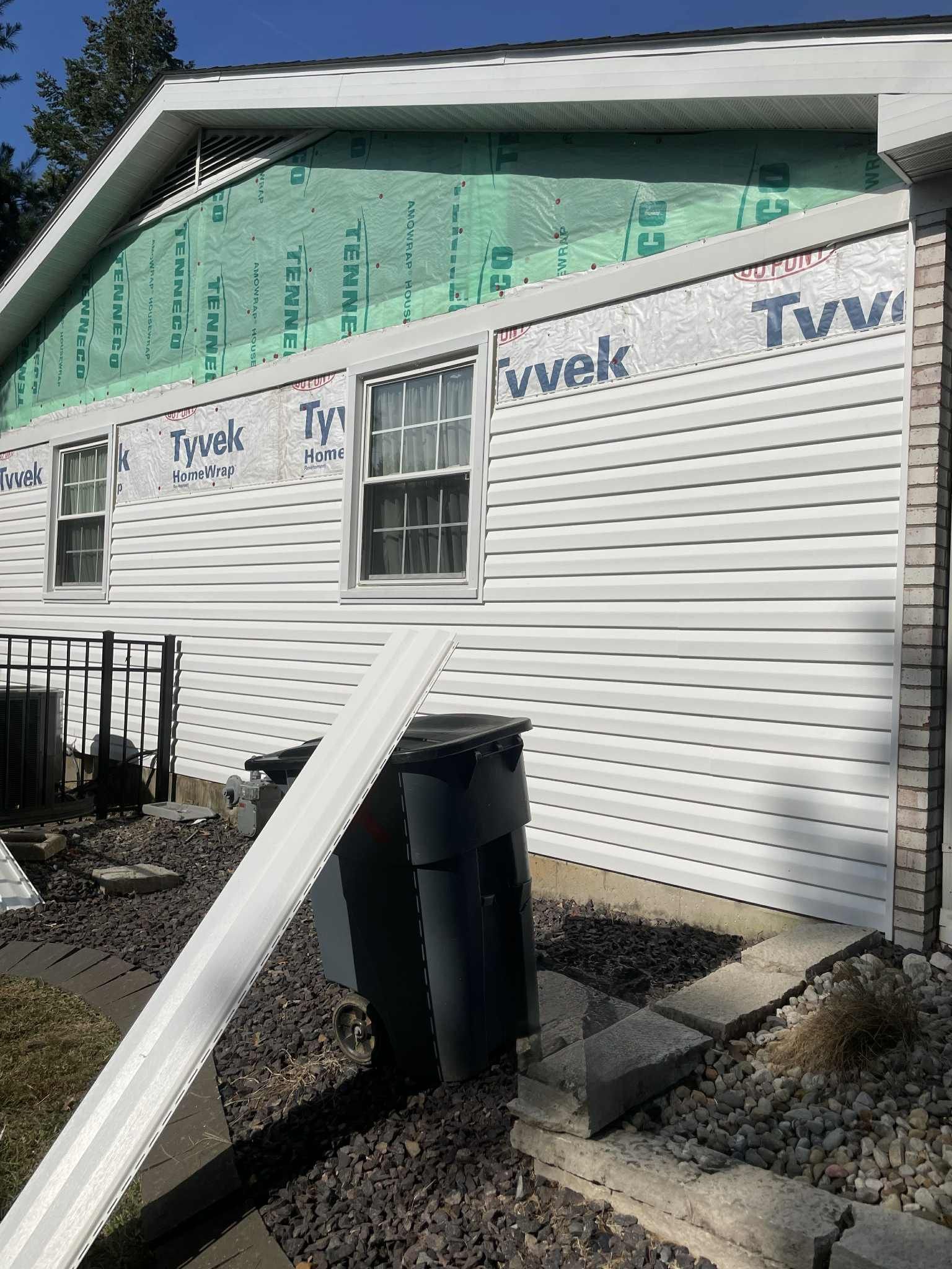 White vinyl siding partially installed on a house with Tyvek wrap visible.