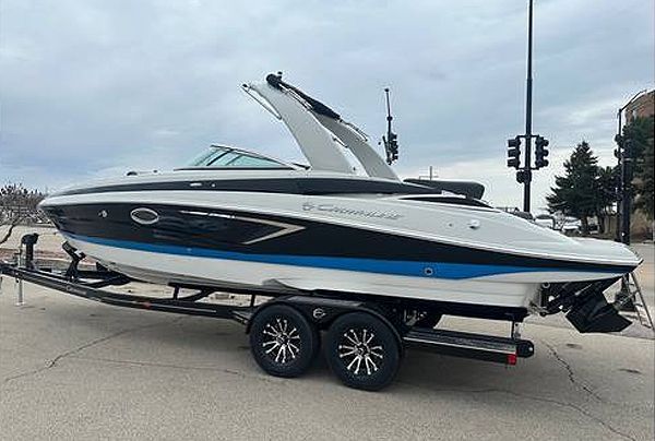 White and black motorboat with blue stripe on a trailer, parked on a street.