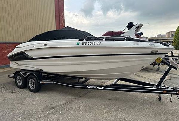 White motorboat on a trailer with black cover, parked outside near a building.