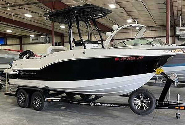 White and black motorboat on a trailer inside a building with a black roof and wheels.