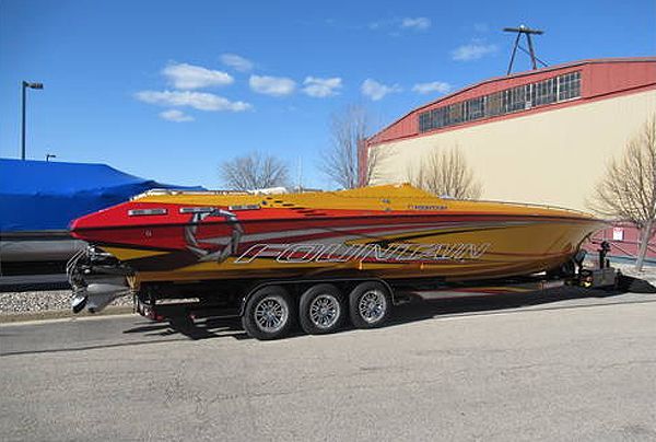 Yellow and red speed boat on a trailer, parked on pavement, next to a building.