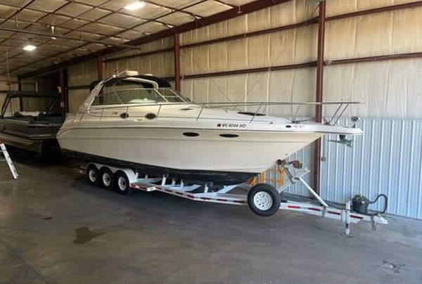 White motorboat on a trailer inside a metal building, with a dark-colored boat to the left.