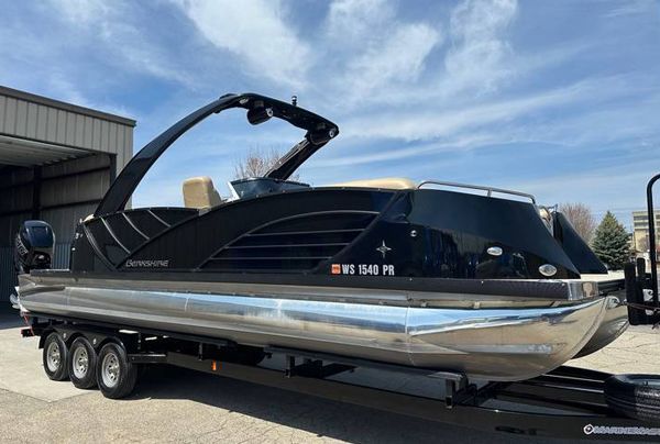 Black pontoon boat on a trailer, under a bright, cloudy sky.