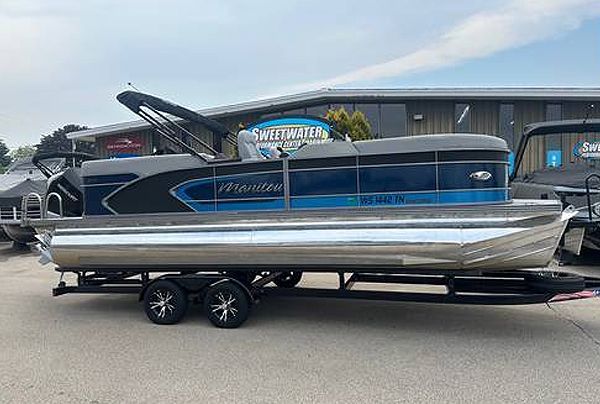 Blue and gray pontoon boat on a trailer, parked in front of a building with a 